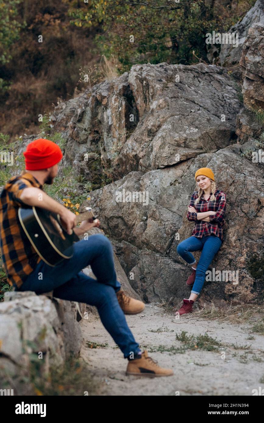a guy in a bright hat plays the guitar with a girl against a background of granite rocks and a river Stock Photo