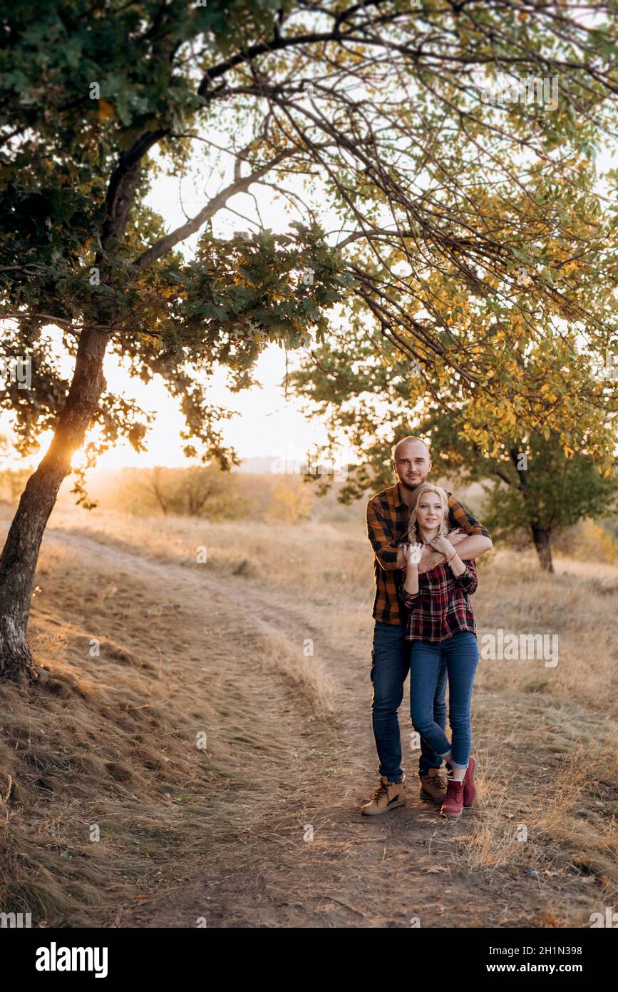 Cheerful guy with a board and a blonde girl for a walk in plaid shirts at sunset Stock Photo