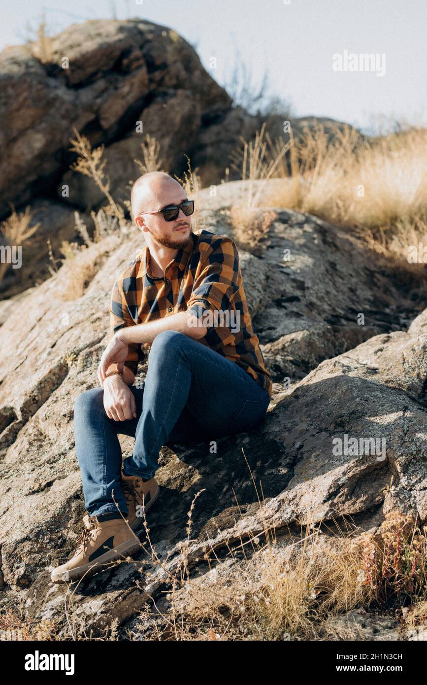 bald guy with a beard in jeans warm shirt and trekking shoes on granite rocks Stock Photo