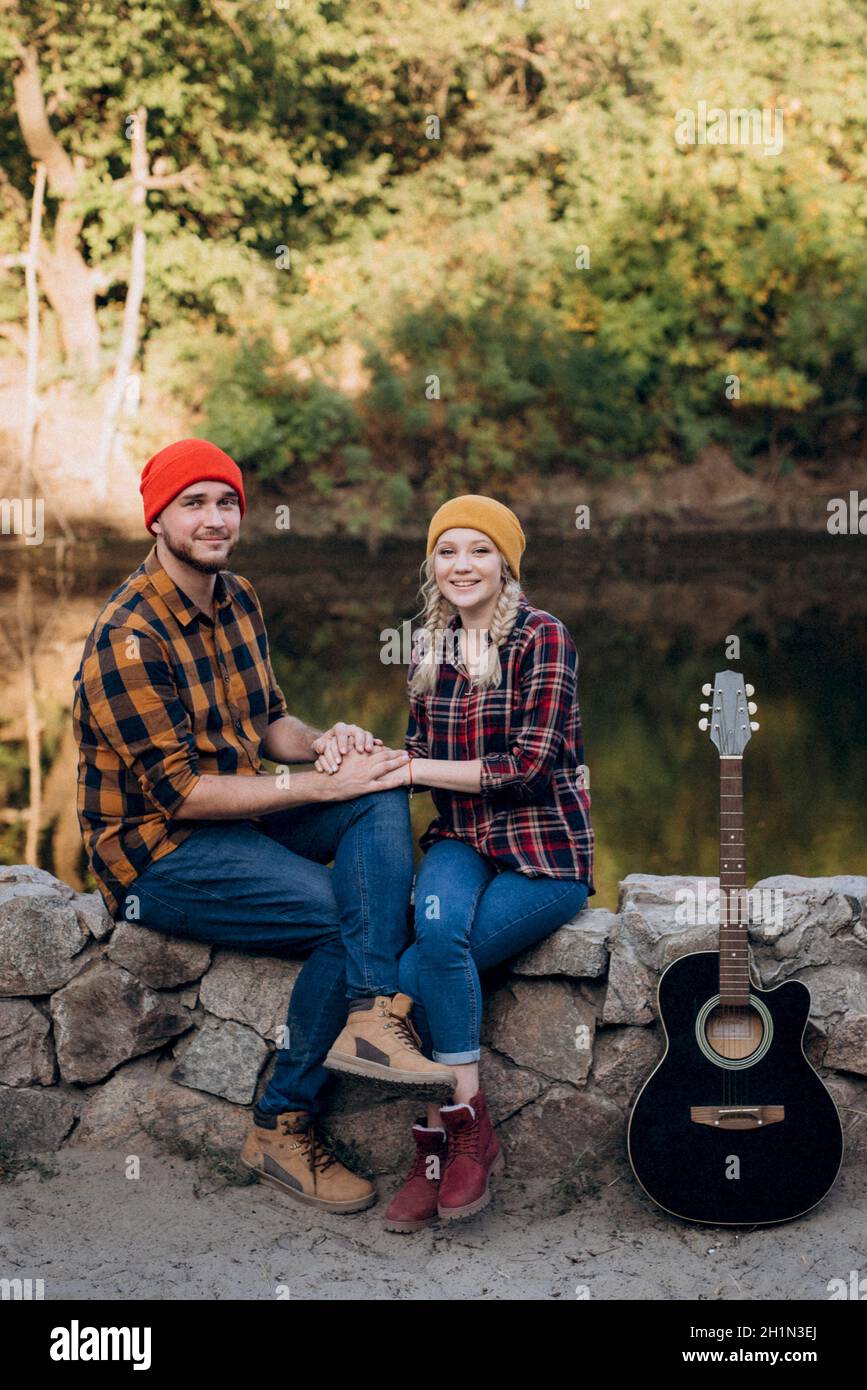 a guy in a bright hat plays the guitar with a girl against a background of granite rocks and a river Stock Photo