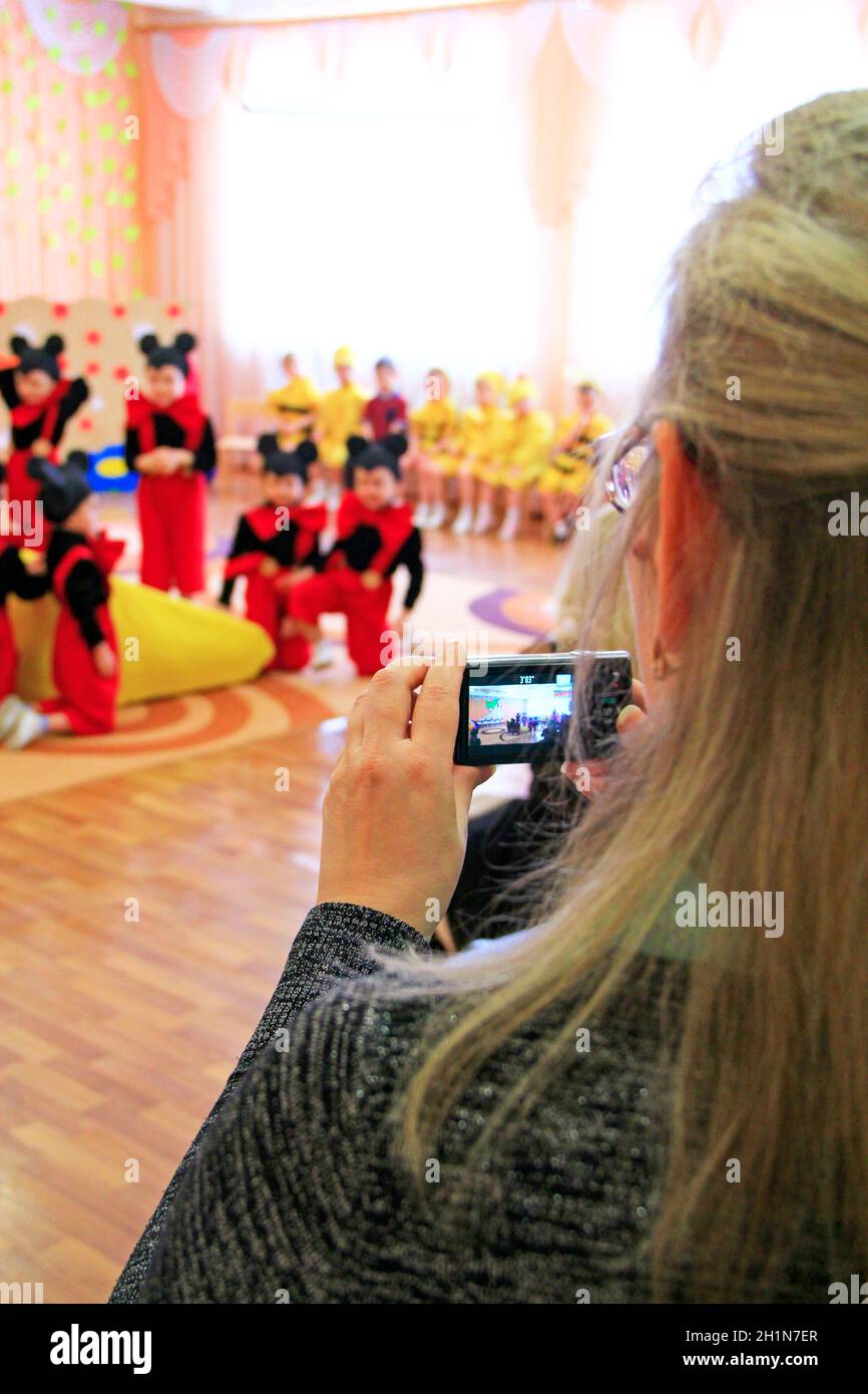 woman photographs matinee in kindergarten. Mother holds digital camera in hands. Shooting for memory. Photo of children. Mother taking baby performanc Stock Photo