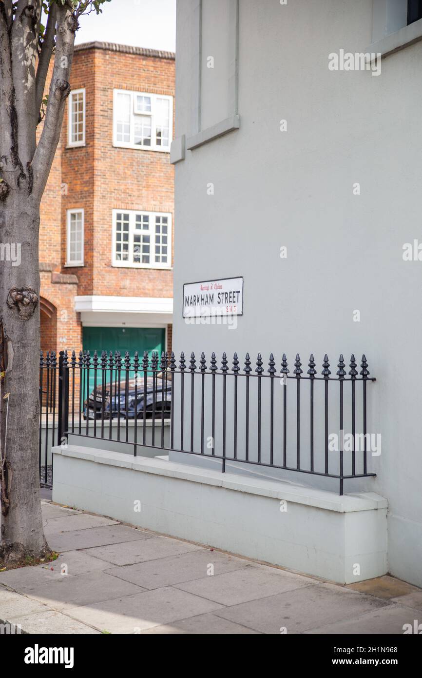Address sign for Markham Street on gray wall behind metal fence and tree. Address sign on British house with brick building and vehicle as background. Stock Photo