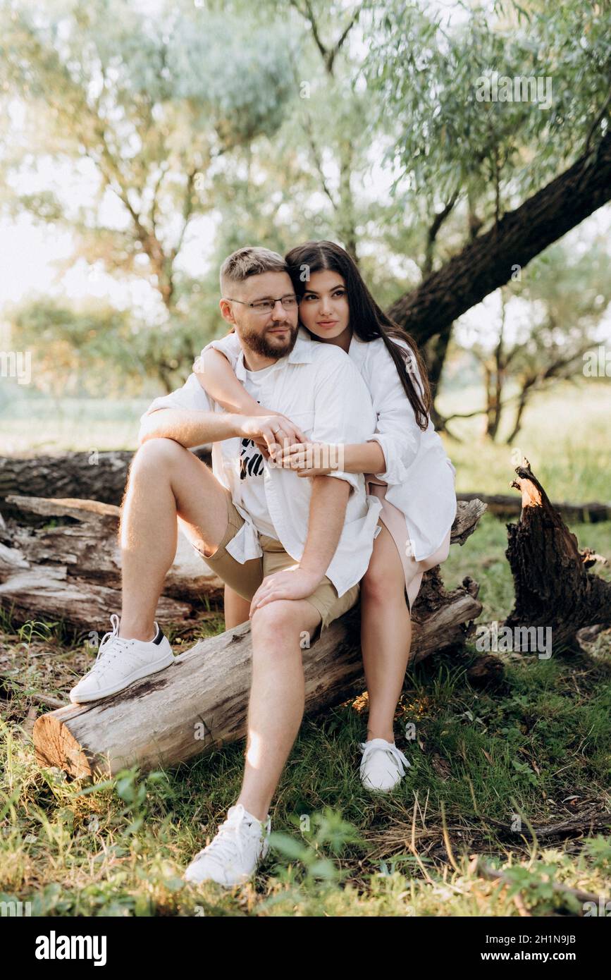 young couple in love a guy with a beard and a girl with dark hair in light clothes in the green forest Stock Photo