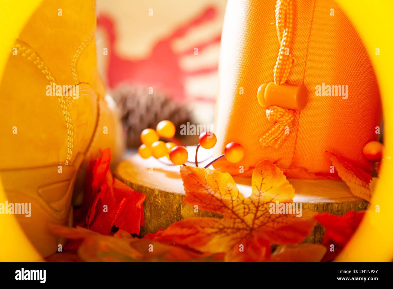 Hunter orange pouch on a wooden slab next to orange and red berries and leaves and a boot with a pinecone and a red hand turkey in the background Stock Photo