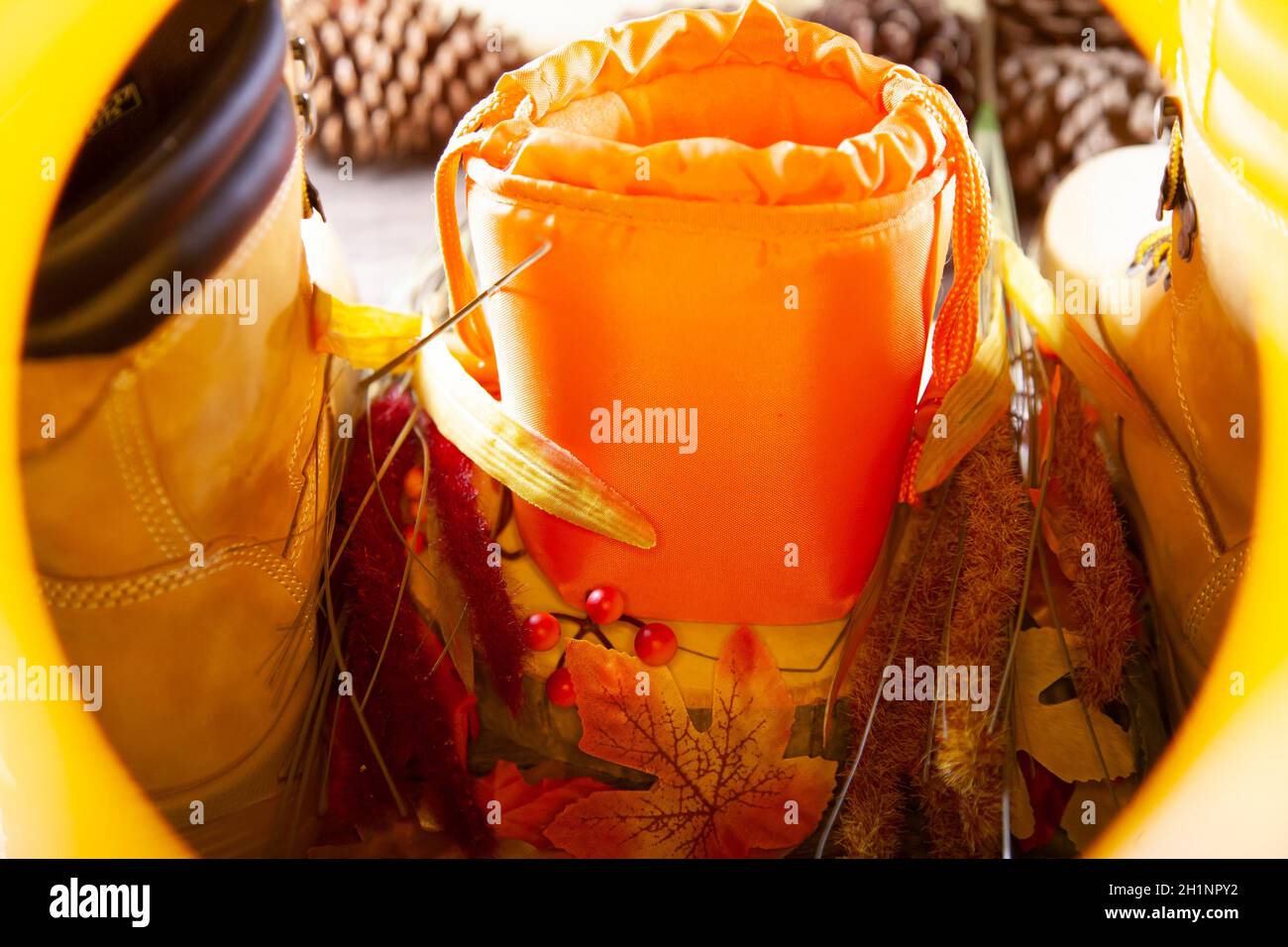A hunter orange pouch on a wooden slab next to orange and red berries and leaves between boots with pinecones in the background Stock Photo