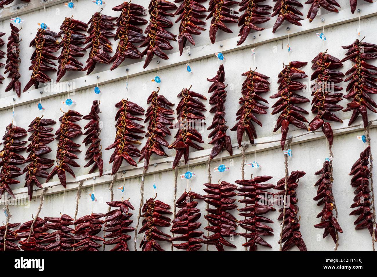 ESPELETTE, FRANCE - CIRCA JANUARY 2021: Strings of PDO Espelette chili peppers drying on white wall. Stock Photo
