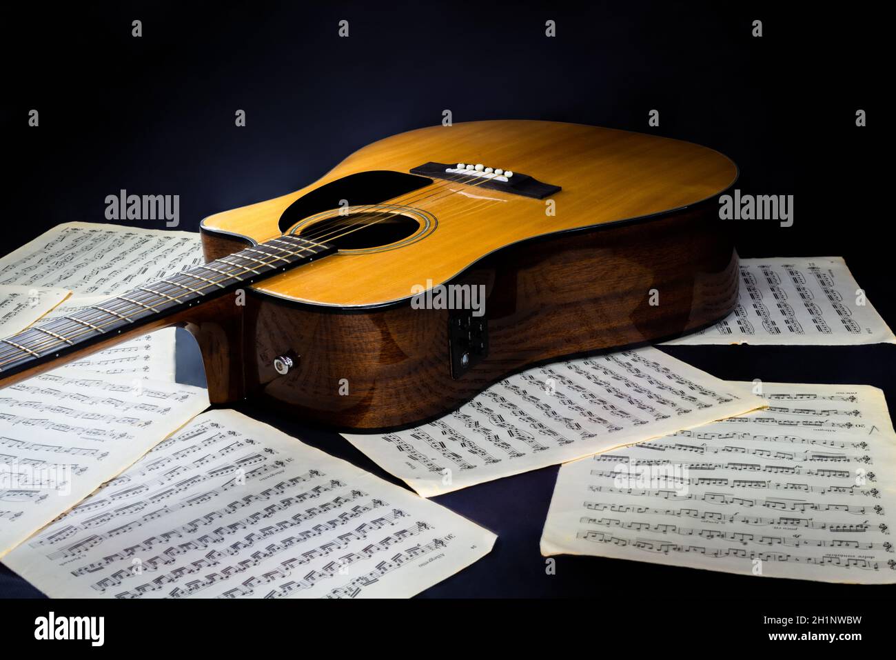 sheets with musical scores and acoustic classical yellow six-string guitar with black pickguard on isolated black background Stock Photo