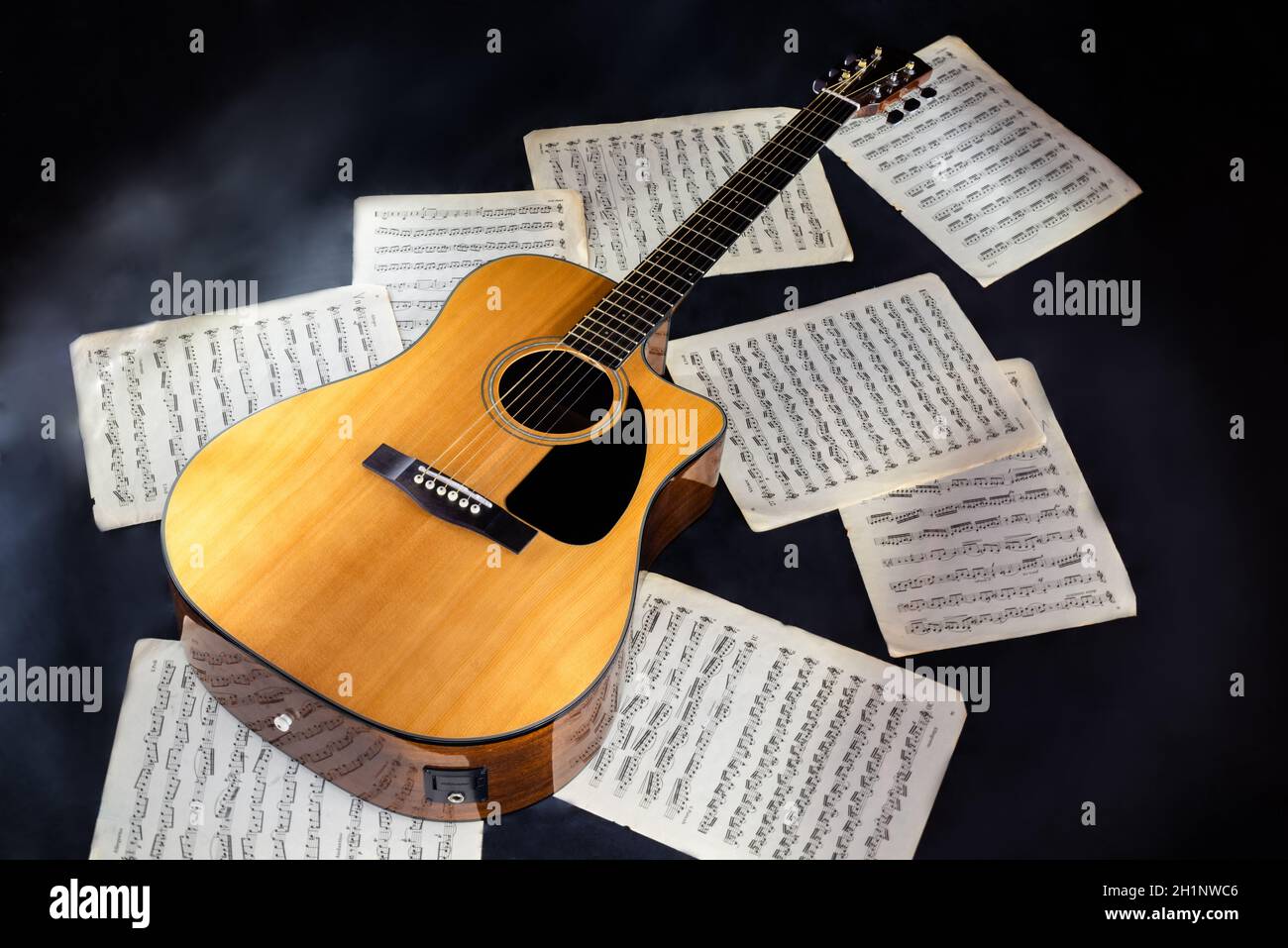 set of sheet music scores and classical acoustic six-string yellow  guitar with black pickguard on isolated black background Stock Photo