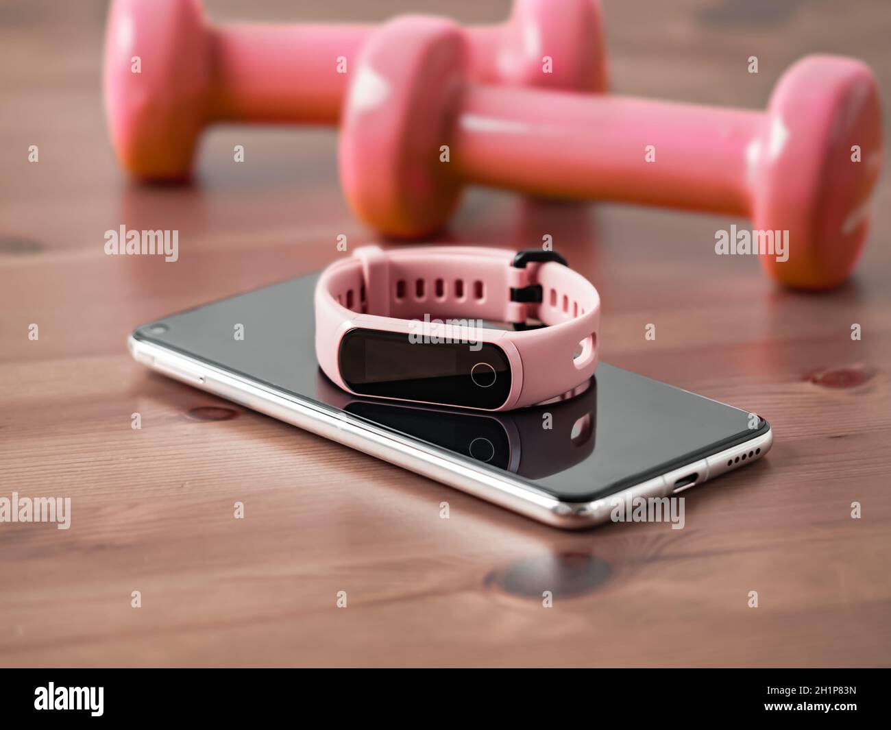 Fitness tracker on smartphone and pink colored dumb-bell on wooden tabletop. Pink female pedometer or wearable device on smartphone with infinity disp Stock Photo