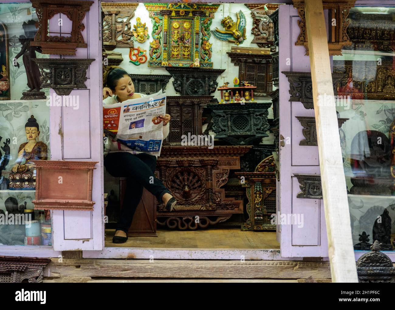 PATAN, NEPAL - CIRCA NOVEMBER 2015: Shopkeeper reading the Kantipur newspaper in her handicraft shop. Stock Photo