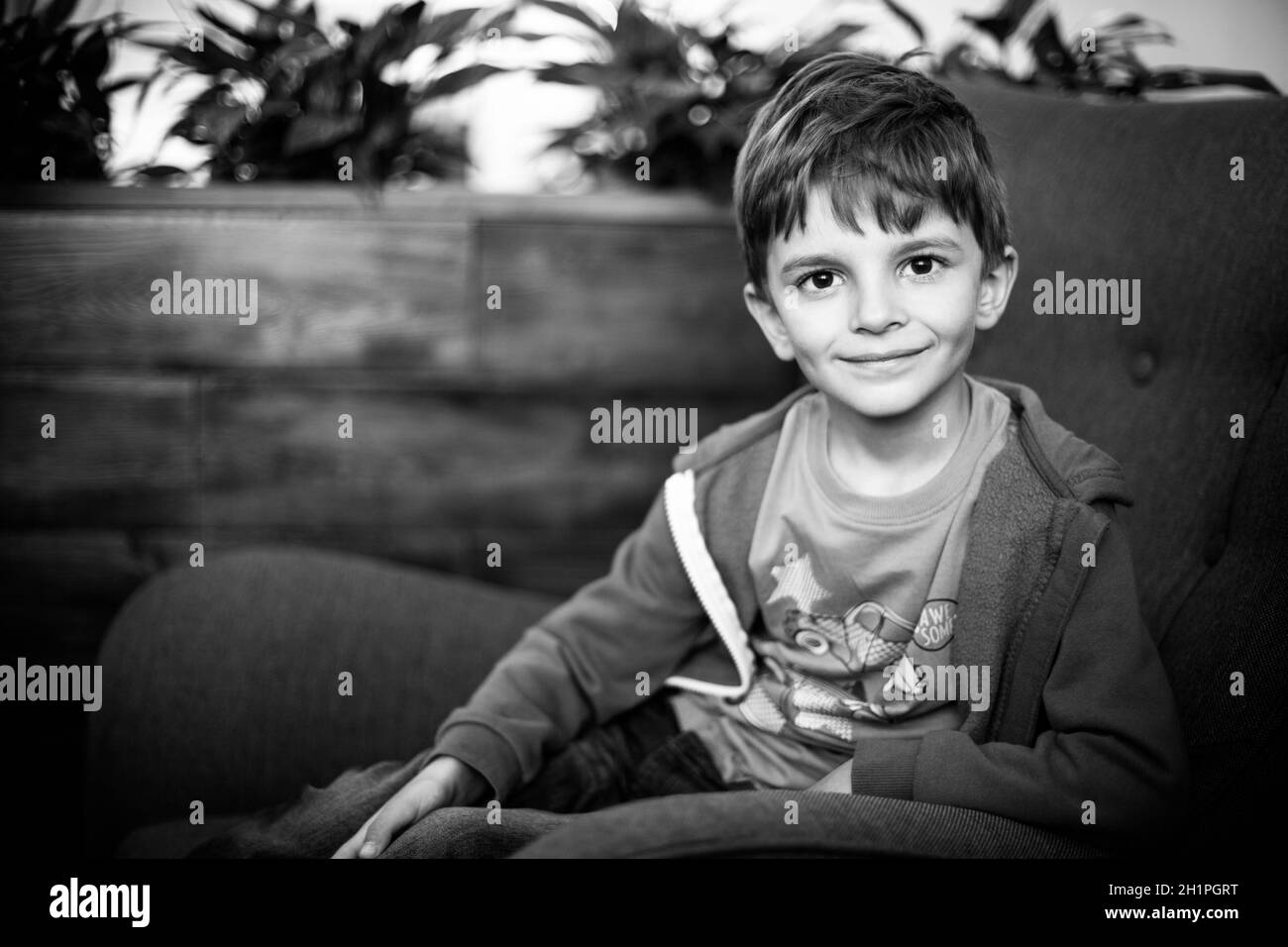 smiling young boy sitting on the sofa looking at camera, black and ...