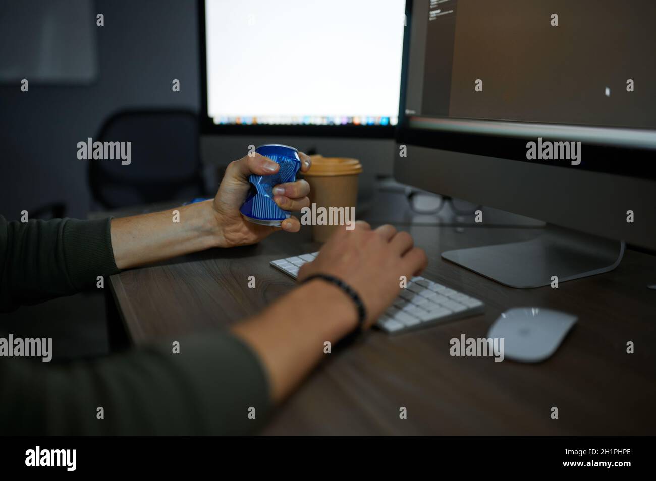 Male internet hacker eats at monitor in dark office. Illegal web programmer at workplace, criminal occupation. Data hacking, cyber security Stock Photo
