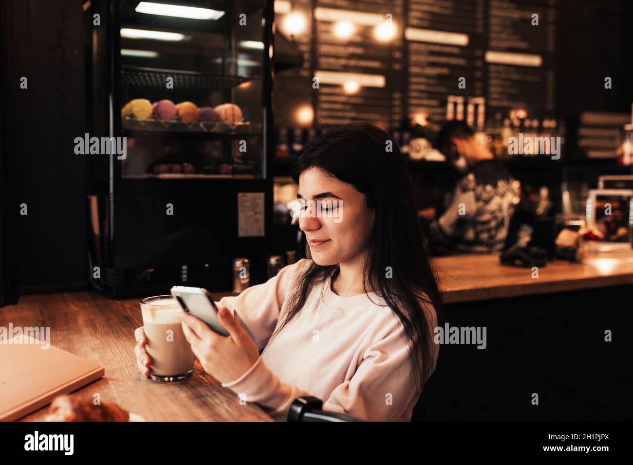 A person sitting in a coffee shop, looking at their phone with a happy expression, surrounded by laptops and coffee cups