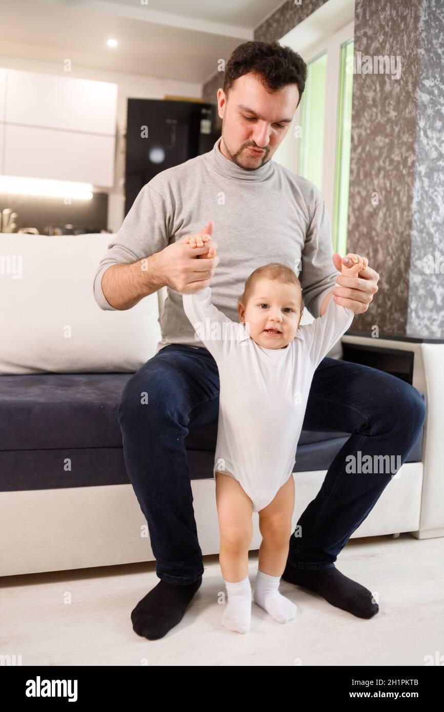 Young father assisting walking his infant son teaching to walk at home ...