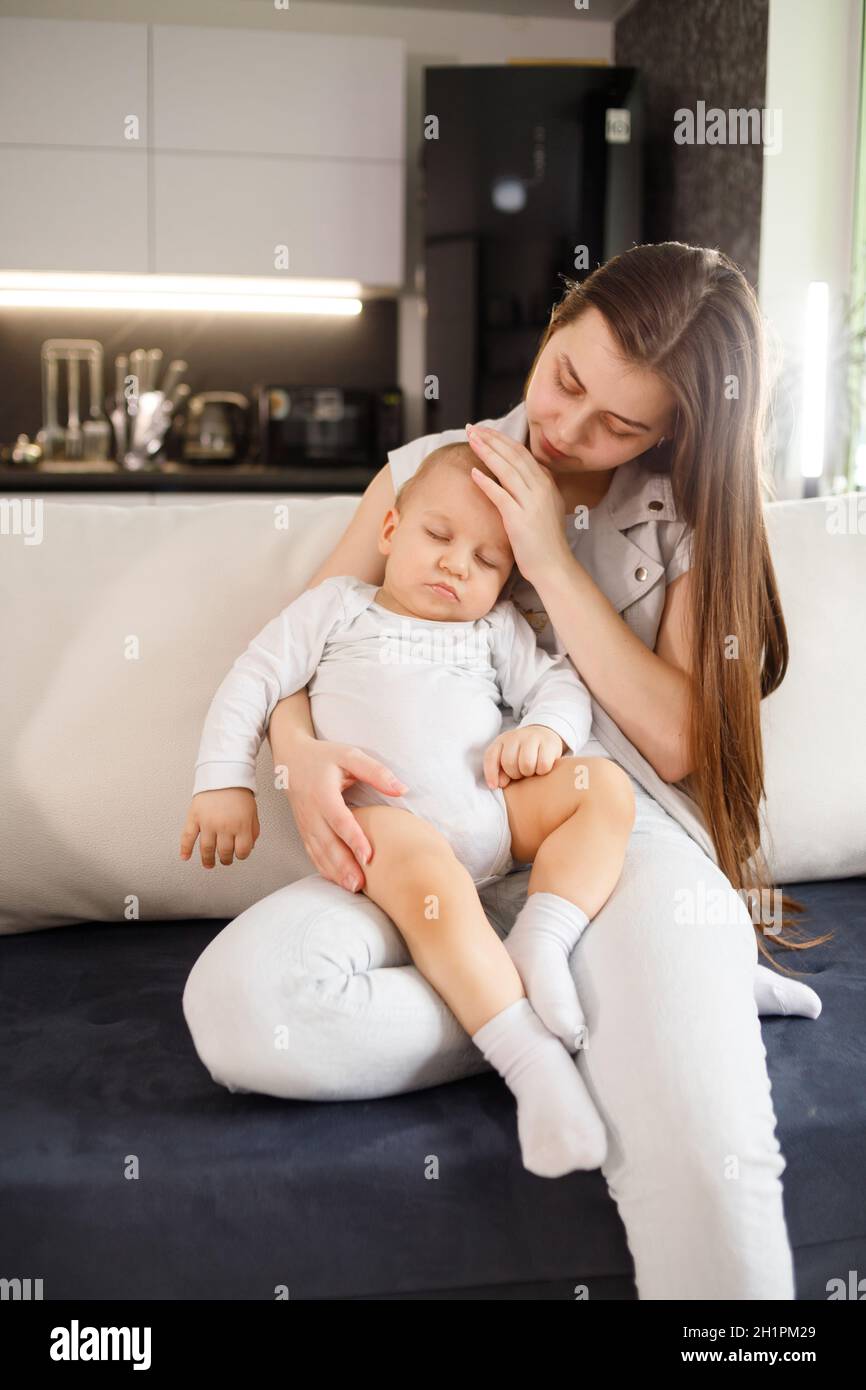 Young mother with sleeping baby on hands on couch at home. Stock Photo