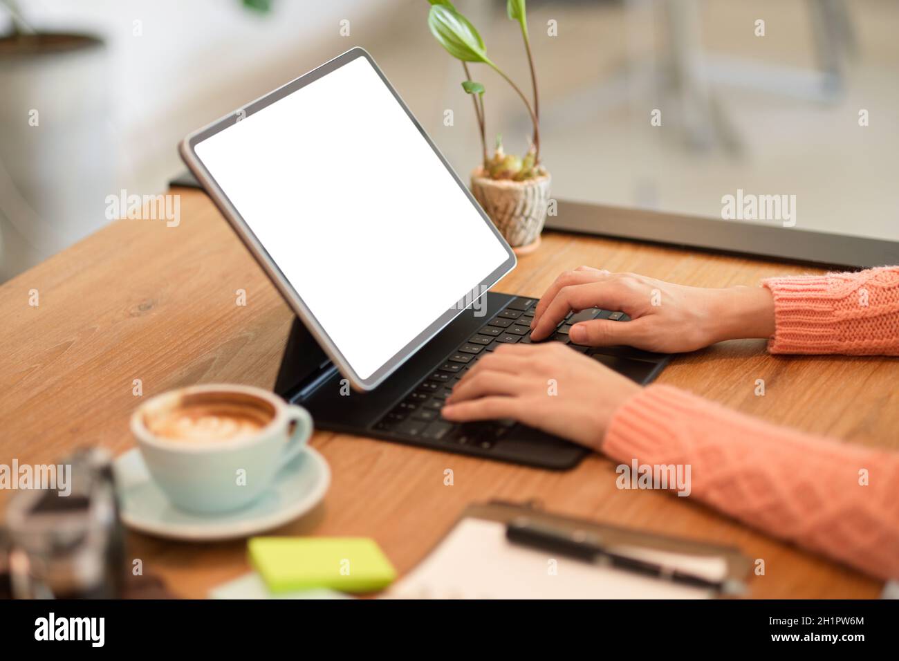 Cropped image of young female freelance travel blogger typing on keyboard, using digital tablet to update her online content. Stock Photo