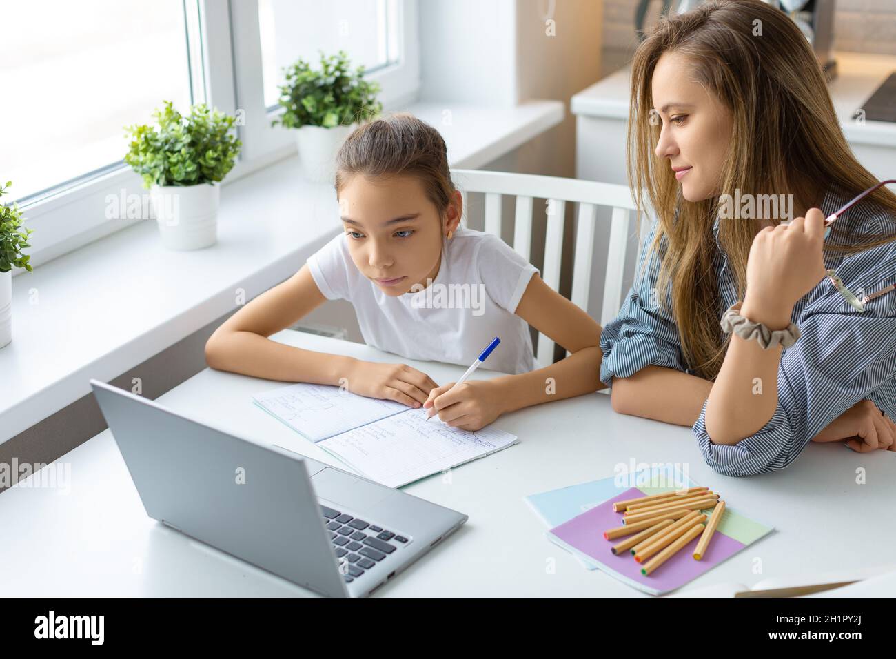 Teenage girl doing homework online at home. Mom closely monitors the correctness of homework. Online education concept. Stock Photo