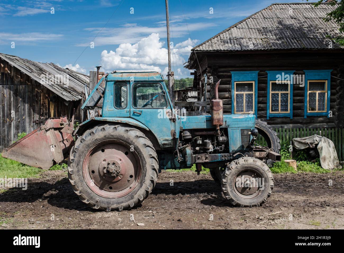 Old Soviet Tractor Next to a Wooden House in the Siberian outback. The village of Bolshoy Balchug is located on the banks of the Yenisei river, 100 km Stock Photo