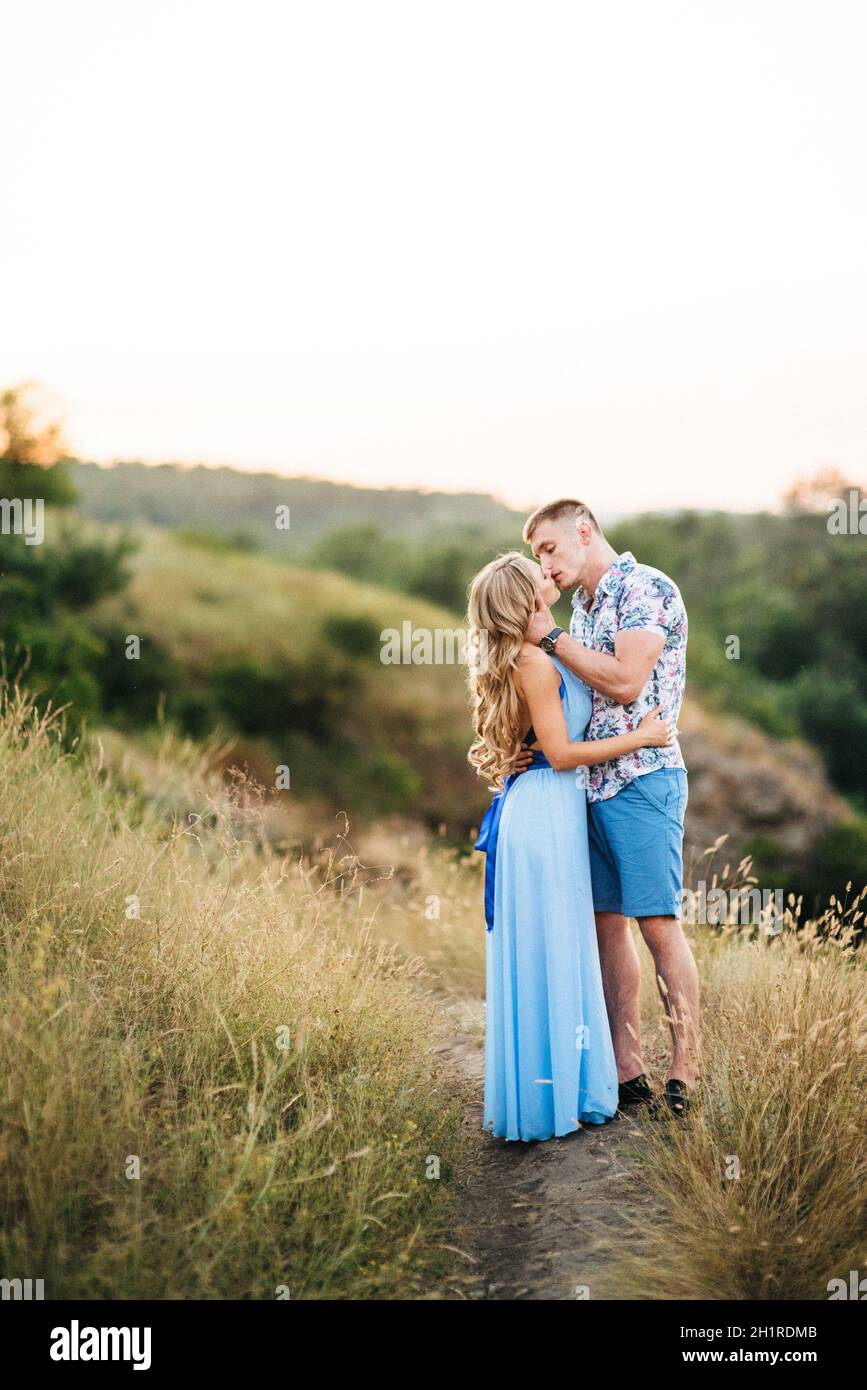 blonde girl with loose hair in a light blue dress and a guy in the light of sunset in nature Stock Photo
