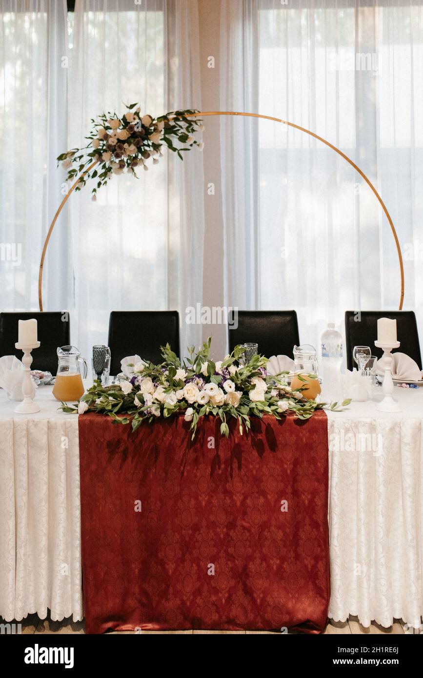 The presidium of the newlyweds in the banquet hall of the restaurant is decorated with candles and green plants, wisteria hangs from the ceiling Stock Photo