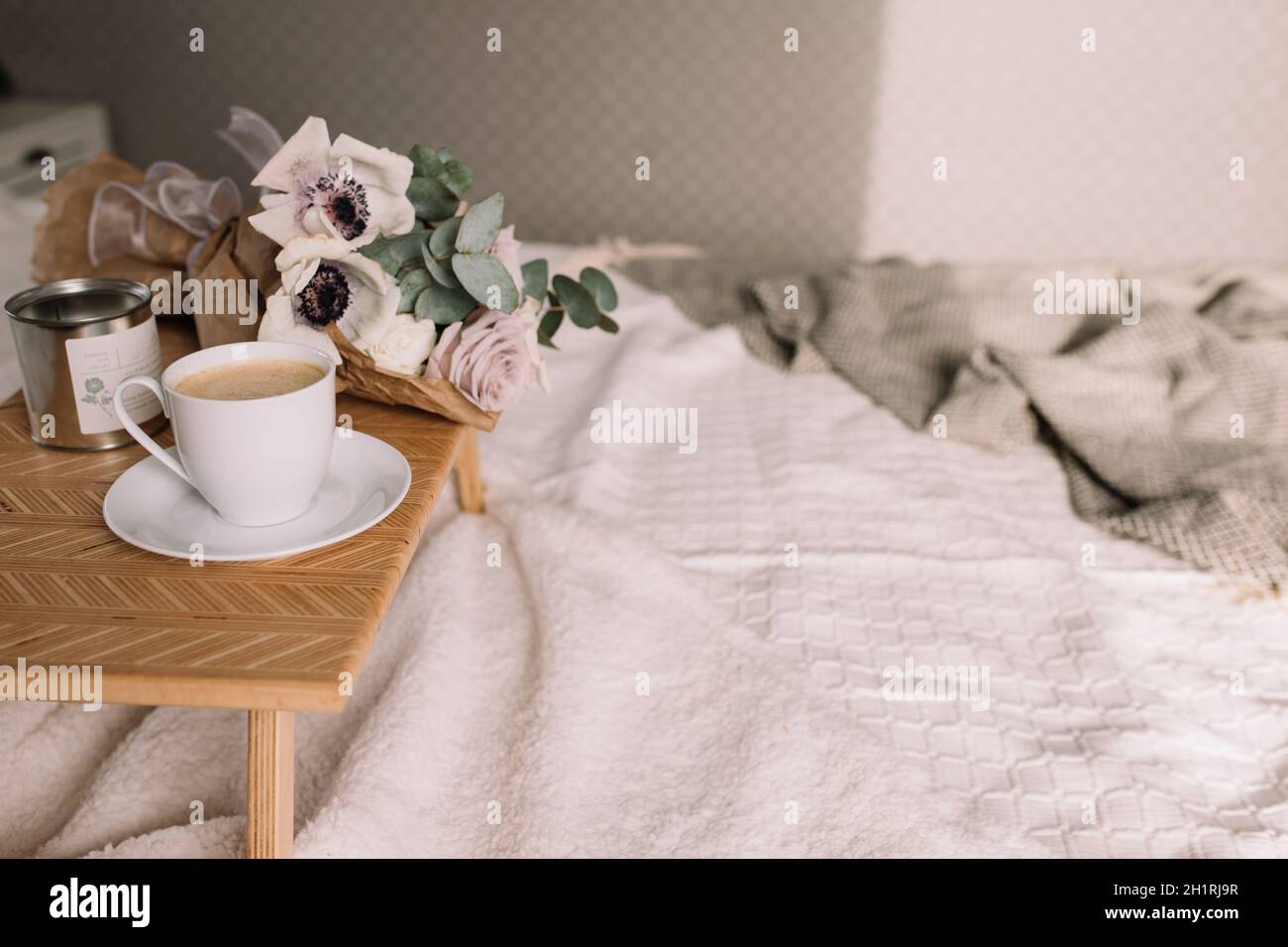 Romantic morning. Wooden coffee table with flowers on bed with plaid, coffee cup, flowers and candles. Lilac roses with eucalyptus and anemones. Inter Stock Photo