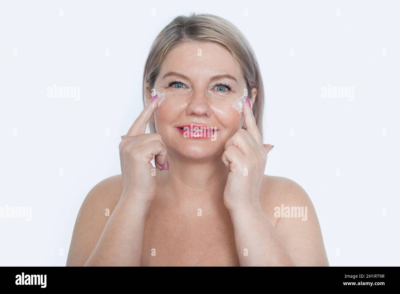 Happy 40s mid aged mature blonde lady applying facial cream on face
