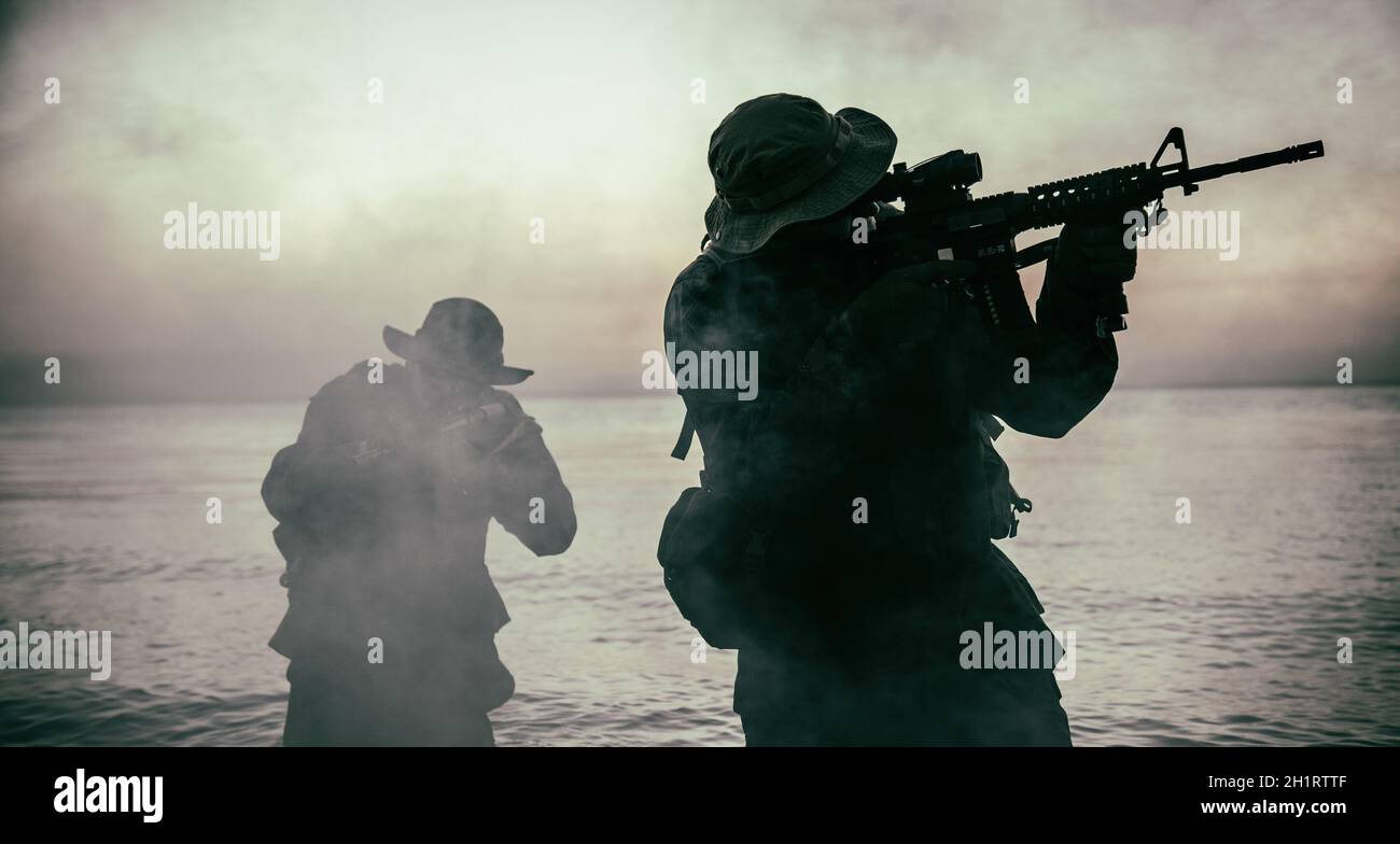 Commando soldiers walking in water, army special operations forces fighters sneaking in darkness, aiming assault rifles and observing shore during amp Stock Photo
