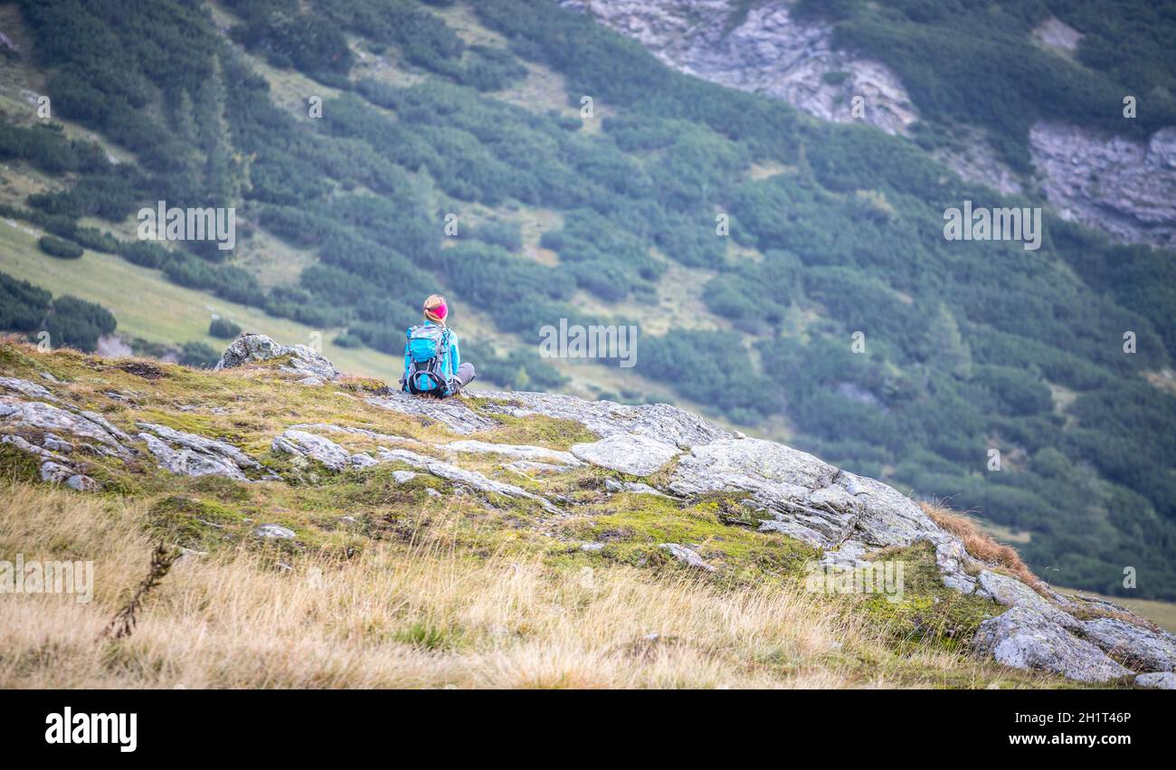 Woman in sportswear and with backpack is sitting on the stony ground and  enjoys the view, in the mountains Stock Photo - Alamy