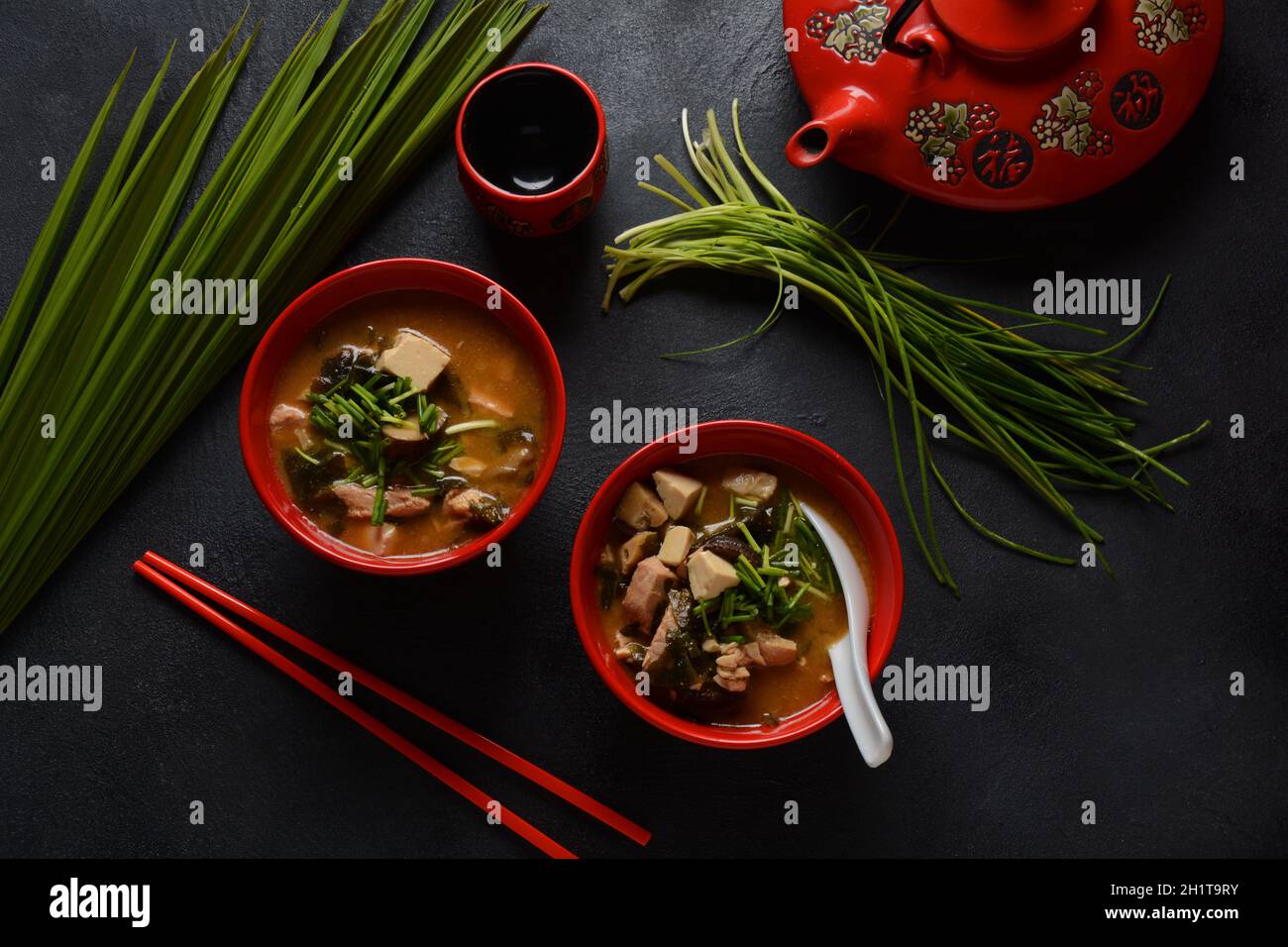 Japanese miso soup in two red Japanese bowls on the black table. Miso