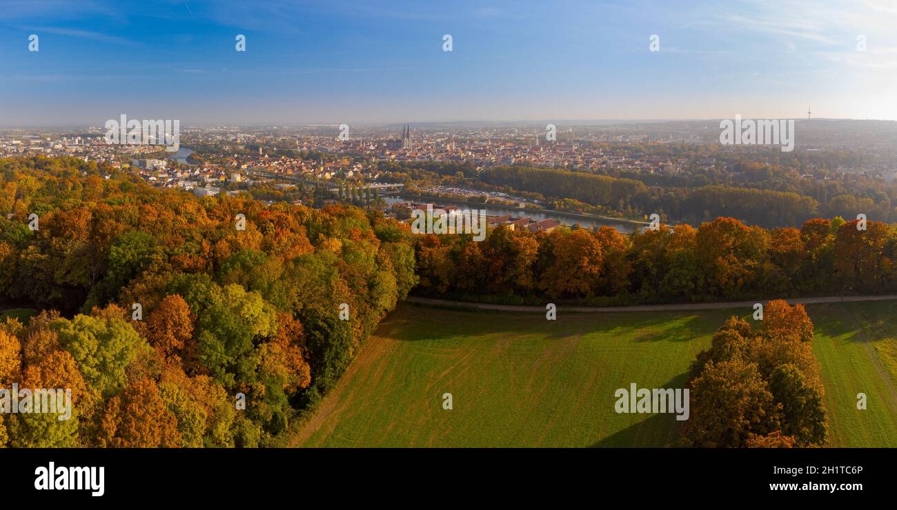 Drone point of view over skyline of Regensburg, Bavaria behind beautiful colorful variegated autumn foliage of deciduous forest on sunny day in Octobe Stock Photo