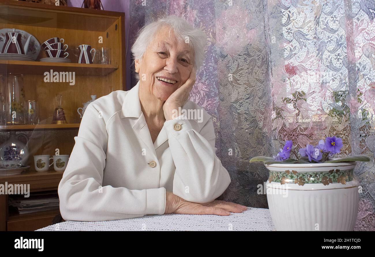 Old lonely happy woman sitting near the window in his house with ...