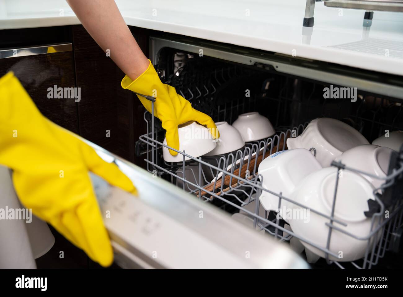 Close up hands of housewife wear yellow gloves loading dishwasher with