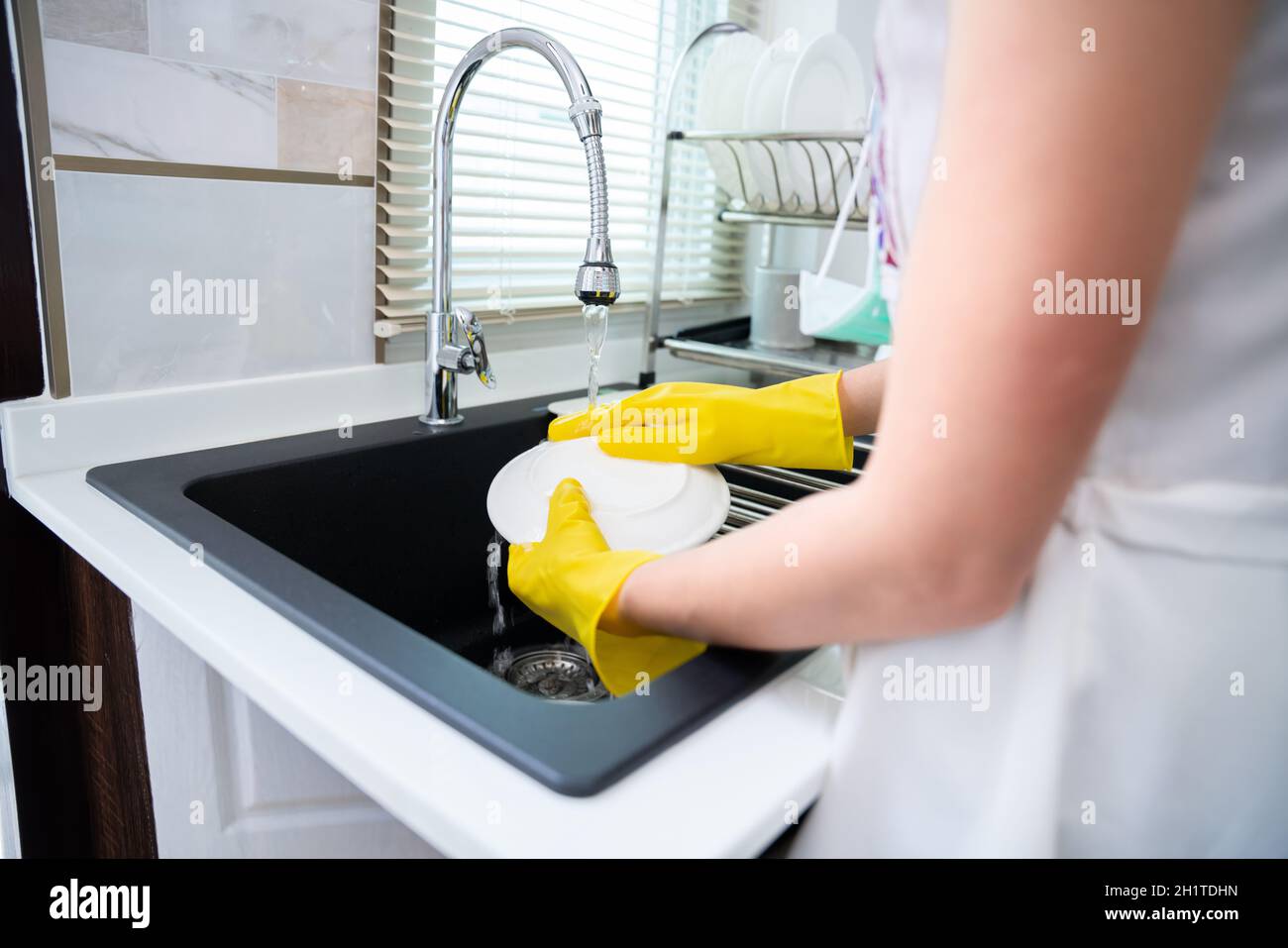 A woman with yellow protective gloves washing her dishes on kitchen sink. Household and home hygiene routine. maid Stock Photo