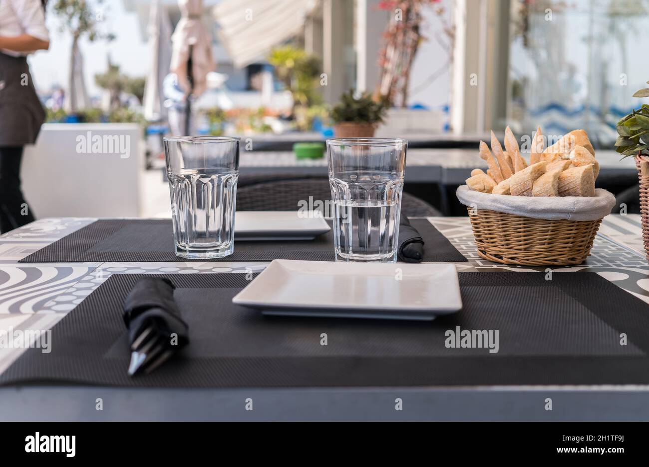 Table prepared on the outside terrace Spanish restaurant, a basket with bread, glasses, plates, and garnished with a plant, Table restaurant terrace Stock Photo