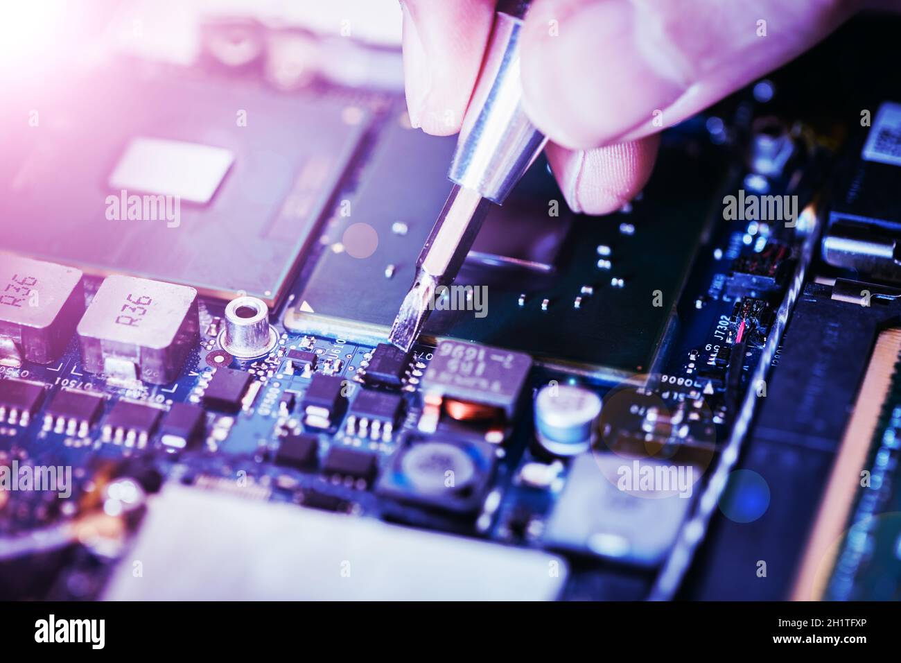 Computer circuit board, hand and screwdriver: Technician is fixing a motherboard. Stock Photo