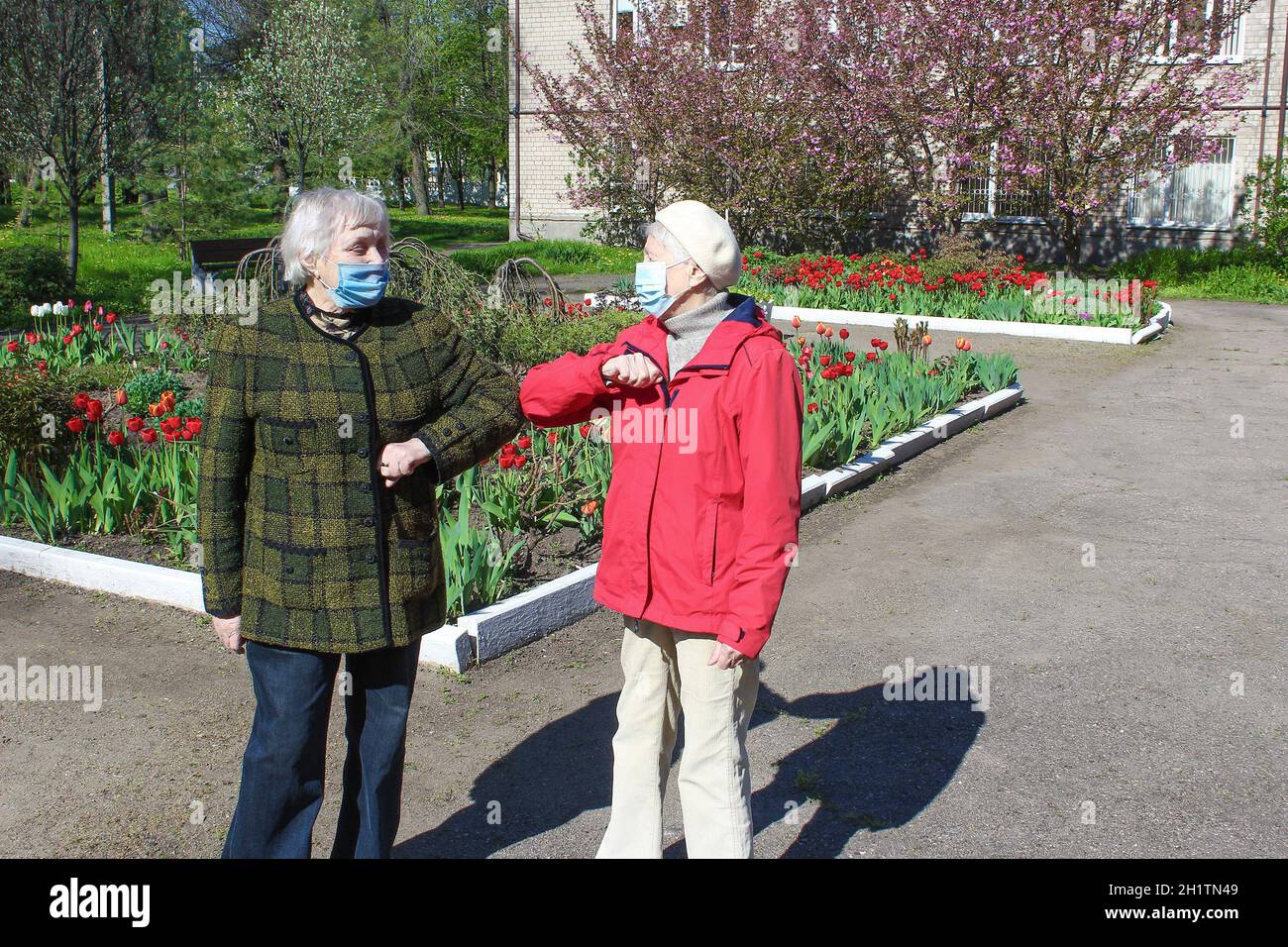 Two senior women wearing facial masks greeting with hand sign, outdoor ...