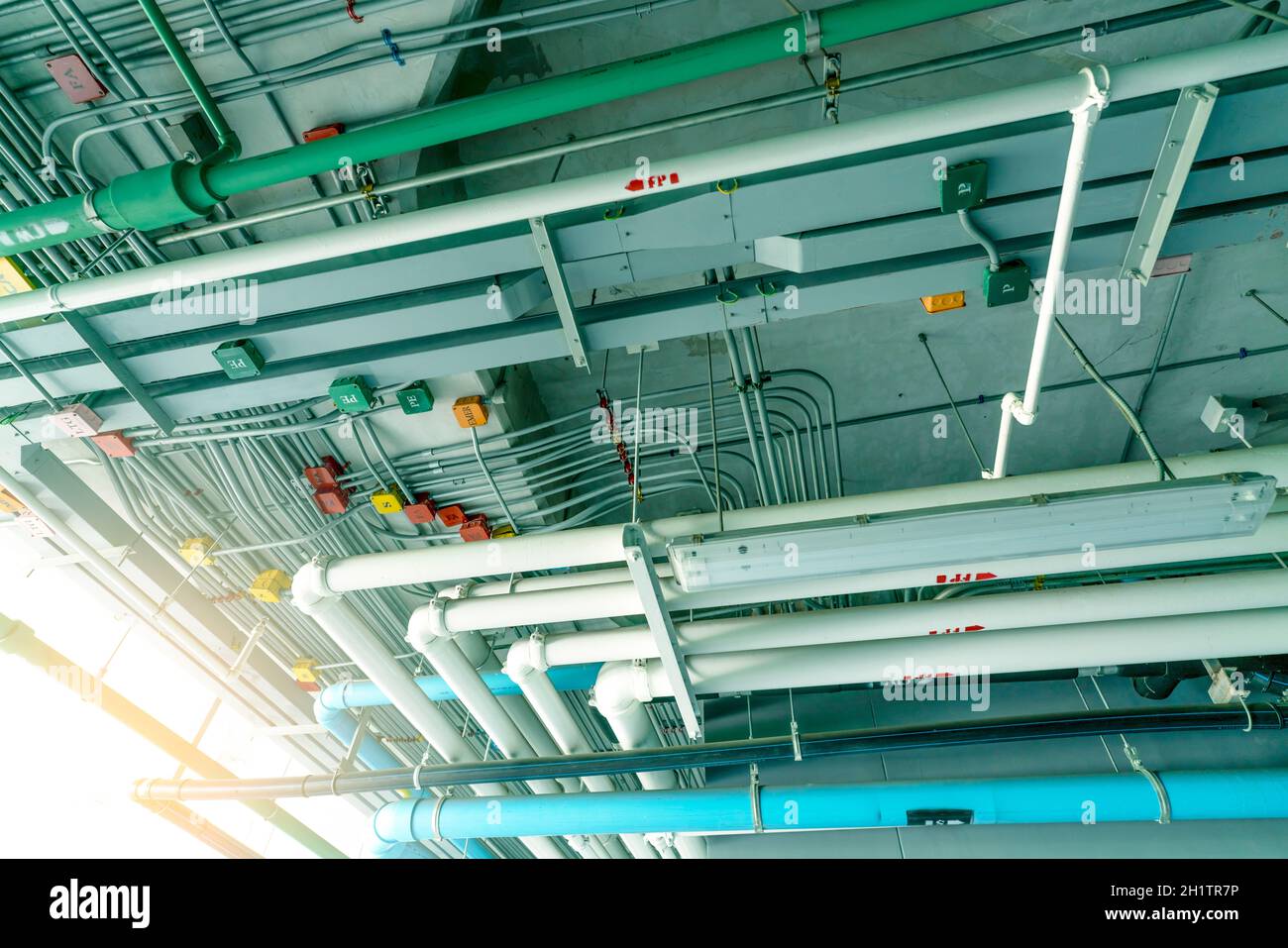 Electrical conduit system and galvanized steel pipe of electric cable installed on ceiling. PVC plastic pipe of drainage system and clean water on ind Stock Photo