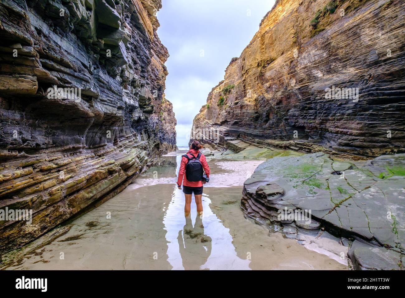 adventure woman explorer walking in the sea between cliffs Playa de las Catedrales Galicia Spain, cathedral beach travel landscape photography camera Stock Photo