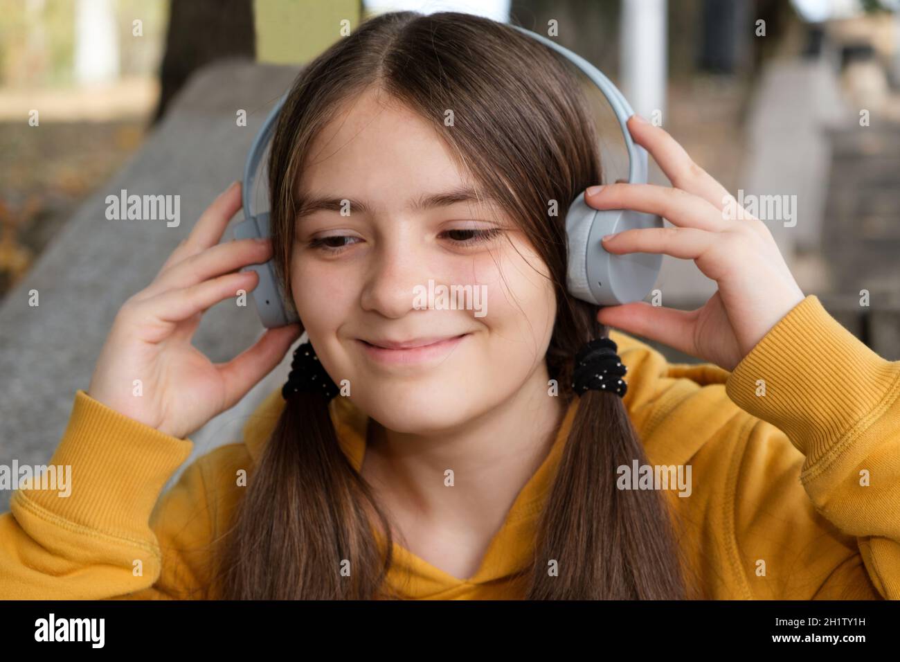 A 13-year-old girl listens to music with headphones and smiles, a large portrait. Stock Photo