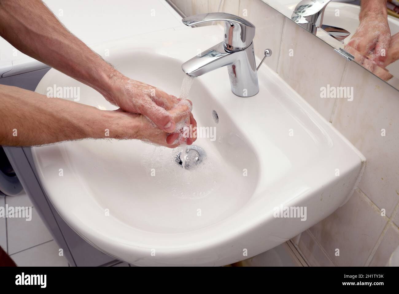 young man washing hands to prevent corony virus disease spreading - soap, water, desinfection whizte sink at home Stock Photo