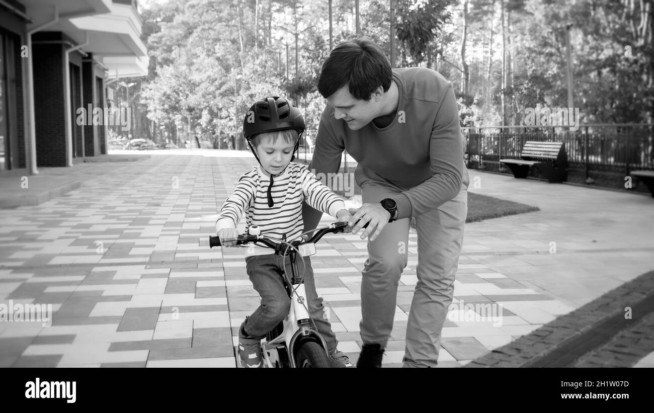 Black and white portrait of young man teaching his son driving his first bicycle. Stock Photo
