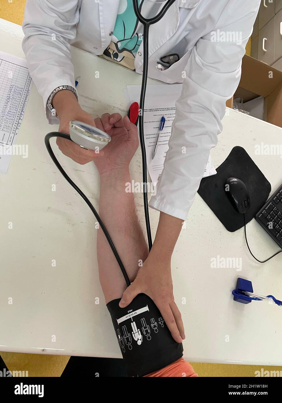 Female doctor in medical facemask measure blood pressure with electronic monitor in hospital. Caring woman GP help examine do checkup of elderly clien Stock Photo