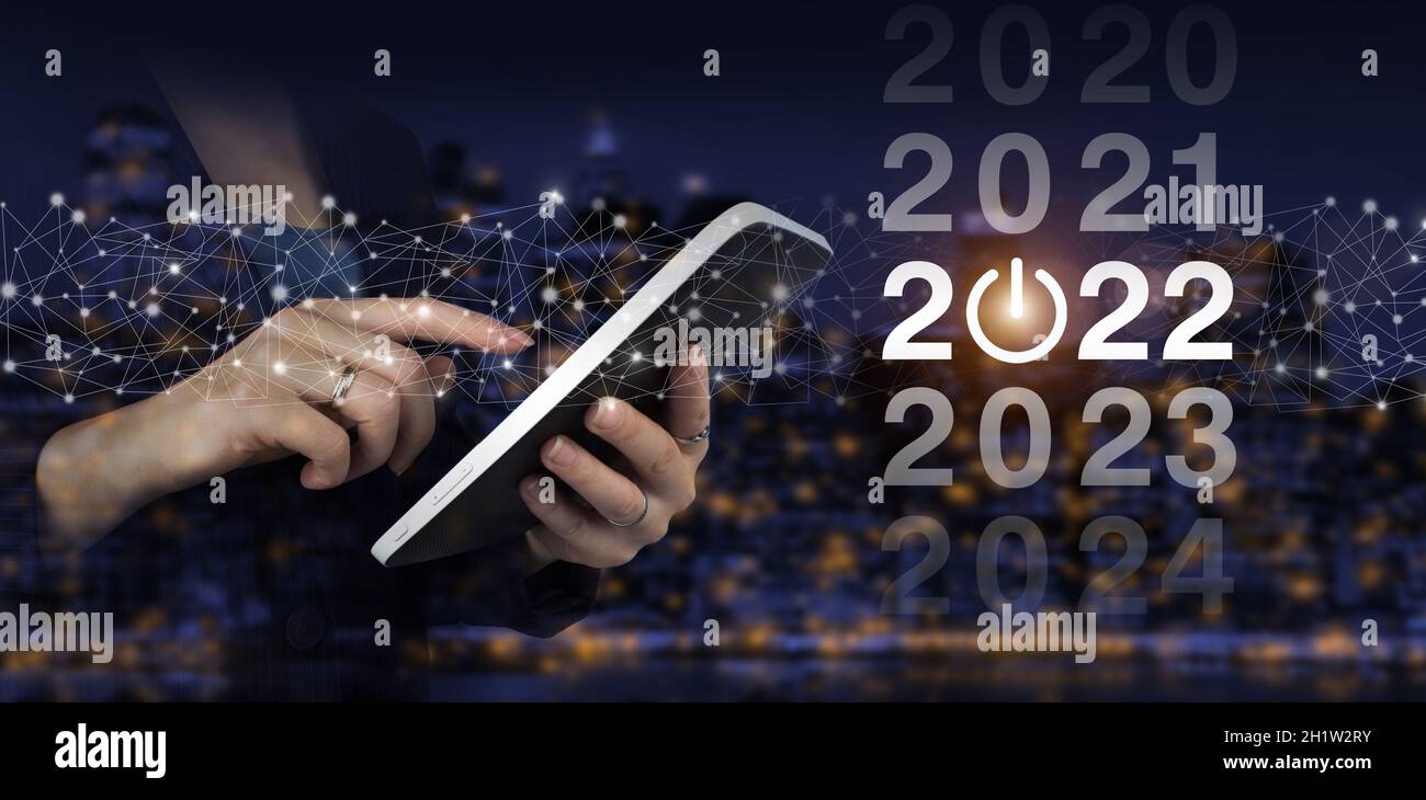 Loading year 2021 to 2022. Start concept. Hand touch white tablet with digital hologram 2022 sign on city dark blurred background. Welcome year 2022. Stock Photo