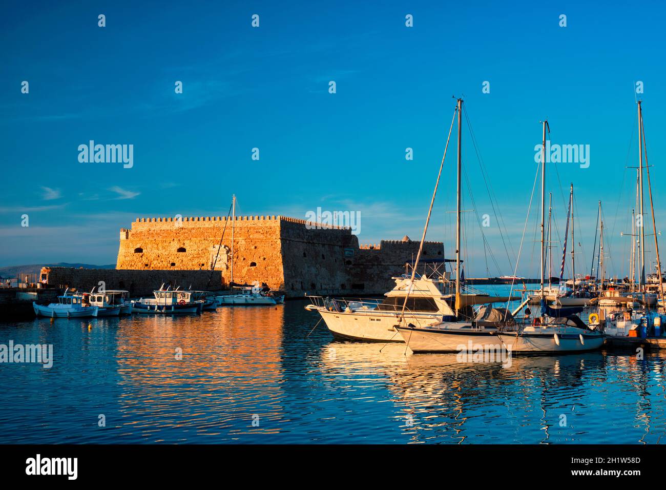 Venetian Fort Venetian fortress of Koules Castello a Mare castle in Heraklion and moored Greek fishing boats in port, Crete Island, Greece on sunset Stock Photo