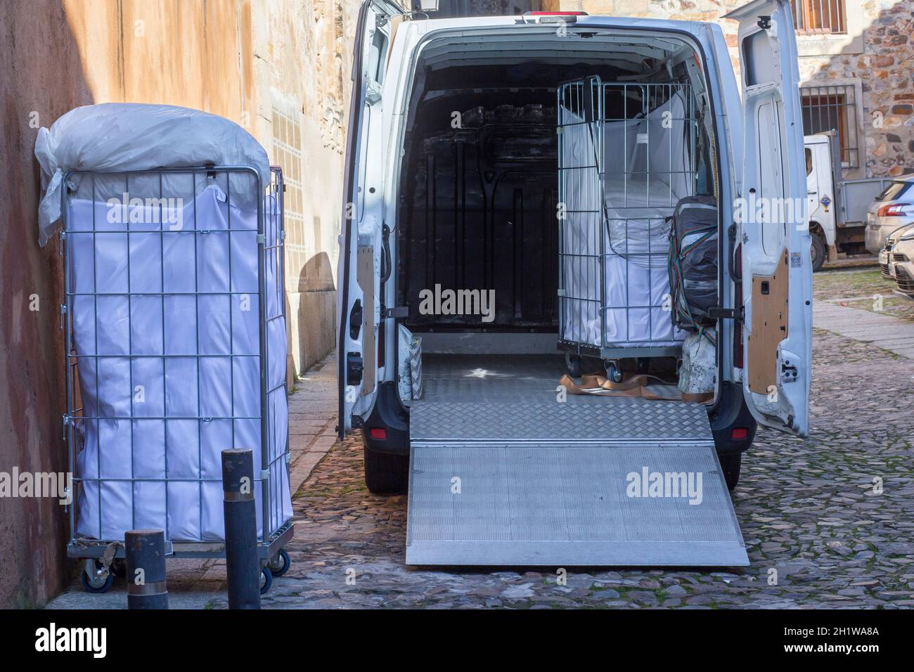 Picking dirt laundry carts. The van equipped with lift ramp is parked in an old town city Stock Photo
