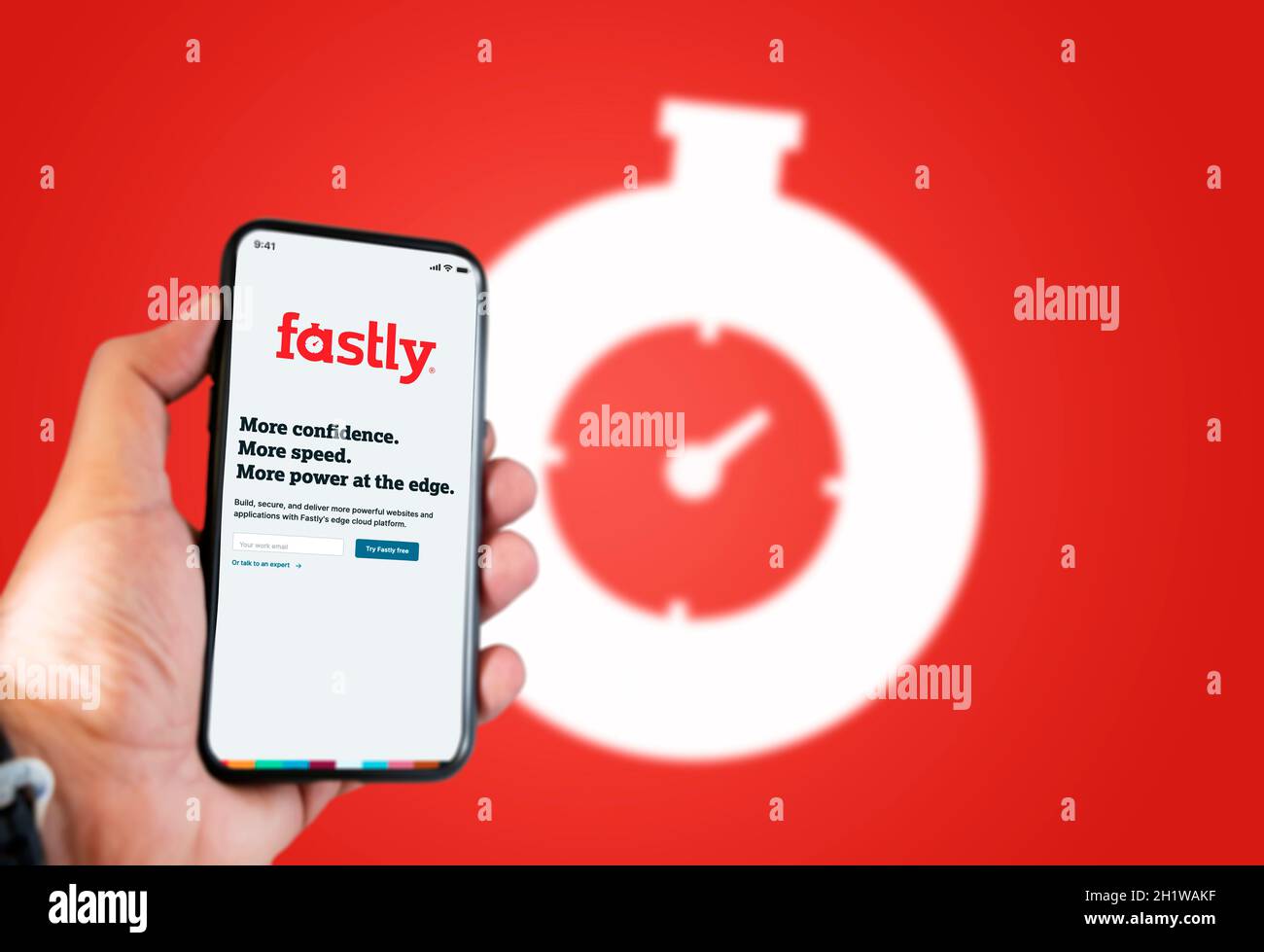 San Francisco, CA, USA, June 2021: A hand holding a phone with the Fastly app on the screen. Red background with blurred Fastly logo. Fastly is an Ame Stock Photo