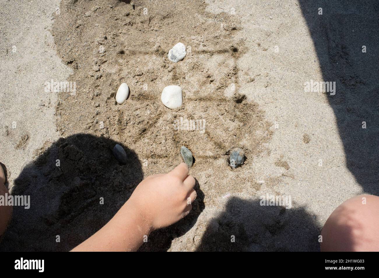 Children playing tic-tac-toe with natural board made with sand marks and beach pebbles. Overhead view Stock Photo