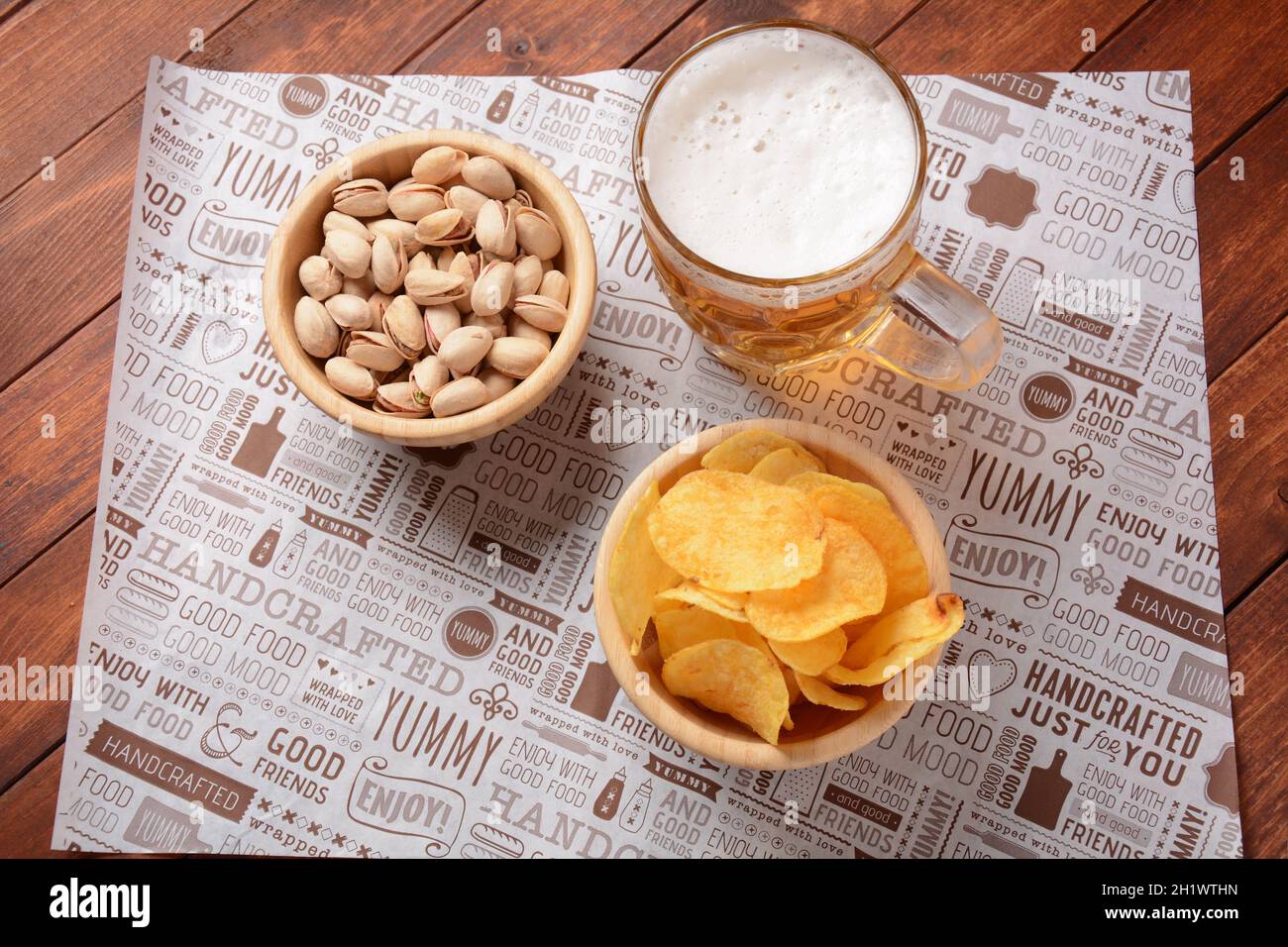 A mug of cold beer with pistachio nuts, and potato chips in wooden bowls. Stock Photo