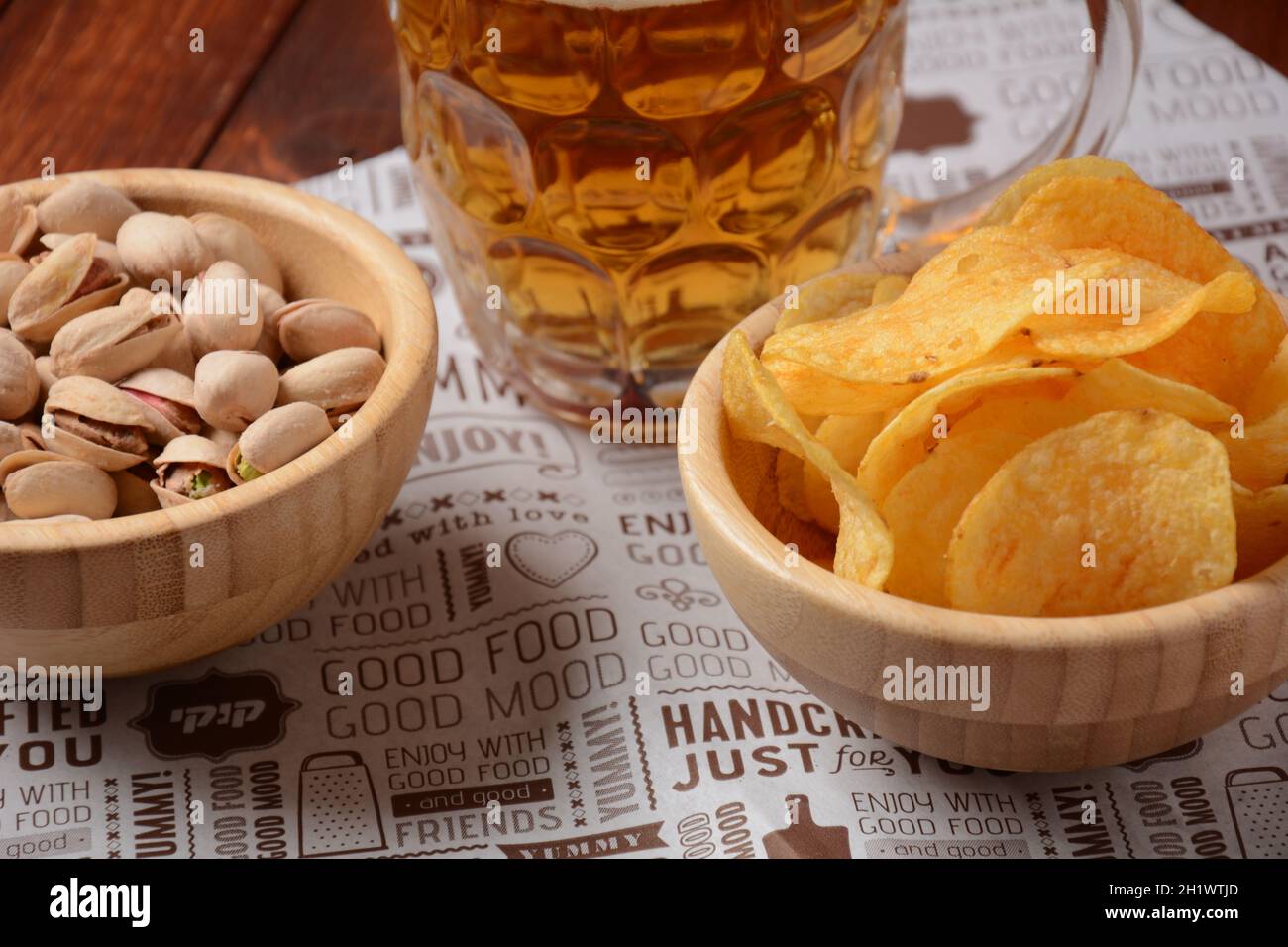 A mug of cold beer with pistachio nuts, and potato chips in wooden bowls. Stock Photo
