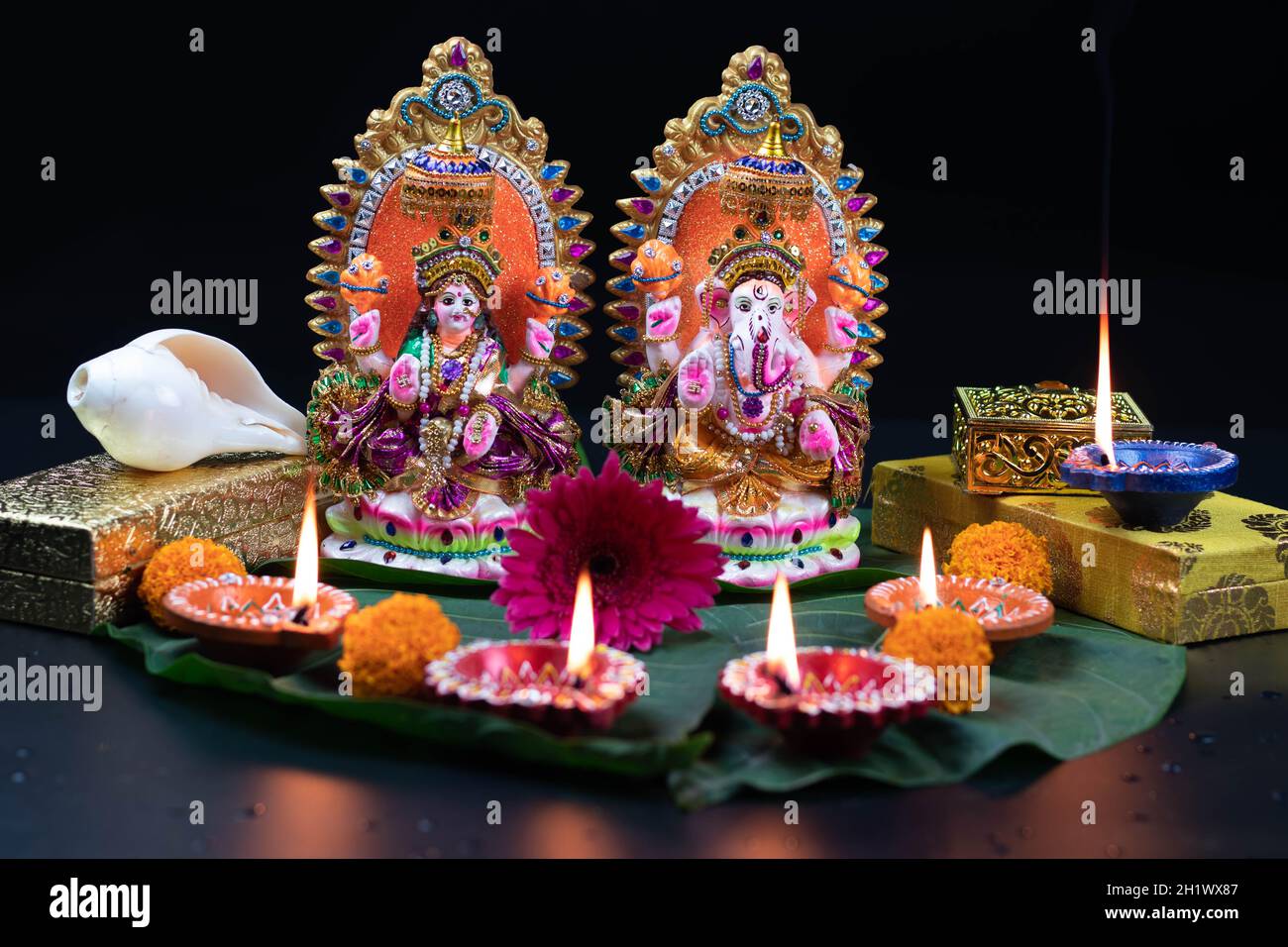 Murti Or Moorti Of Bhagwan Ganesha Ganpati, Mata Lashmi Or Devi Laxmi Maa. Gift Boxes Flowers And Shankh And Diya Deep Dia Lit On Green Leaf. Theme Fo Stock Photo